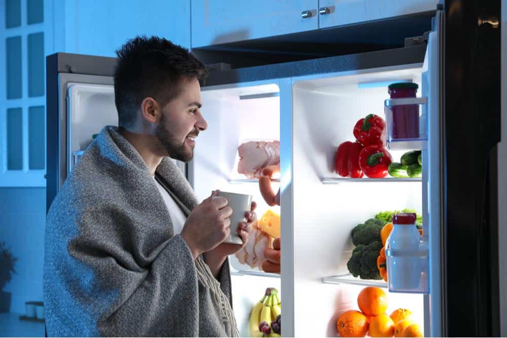 Photo of a man with a blanket peering into a refrigerator