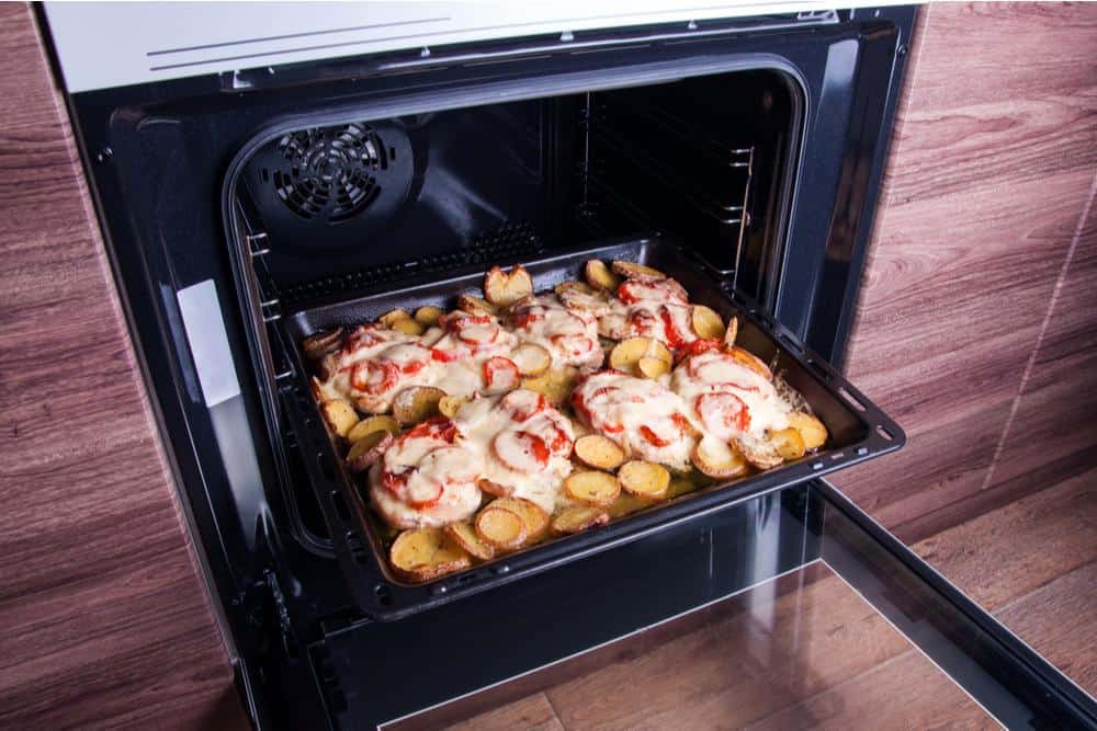 Photo of an oven with potatoes cheese and tomatoes on baking sheet