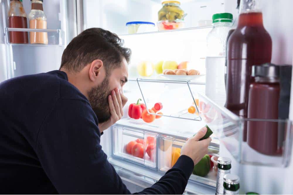 Photo of Man Covering Mouth and Nose Near Bad Smelling Fridge