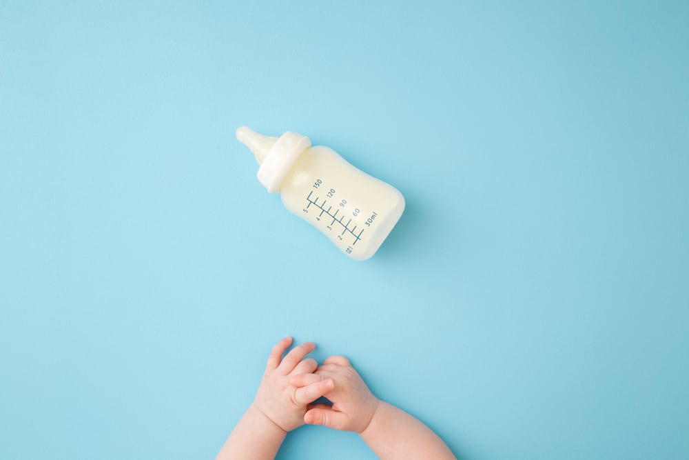 Photo of a baby bottle with a baby's arms nearby