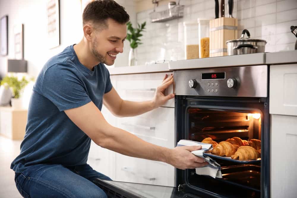 Photo of a man removing croissants from an electric oven