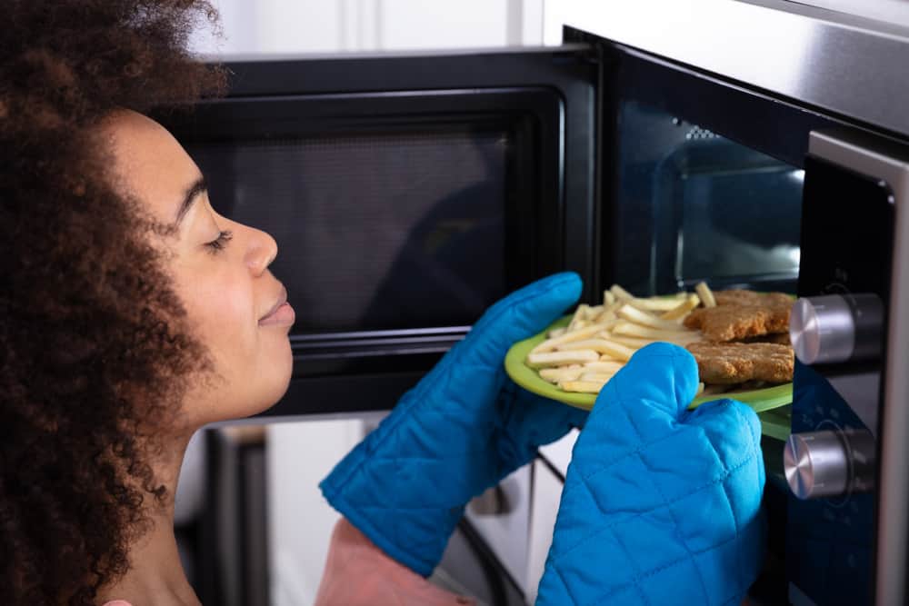 Photo of a woman using oven mitts to remove food from microwave