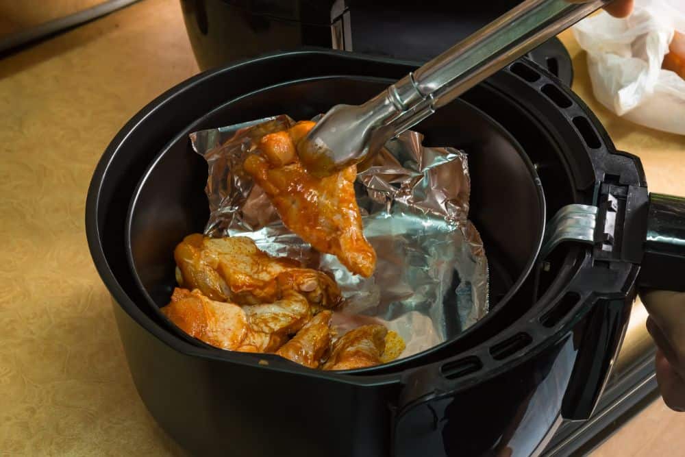 An air fryer with chicken wings in it and dishwasher.