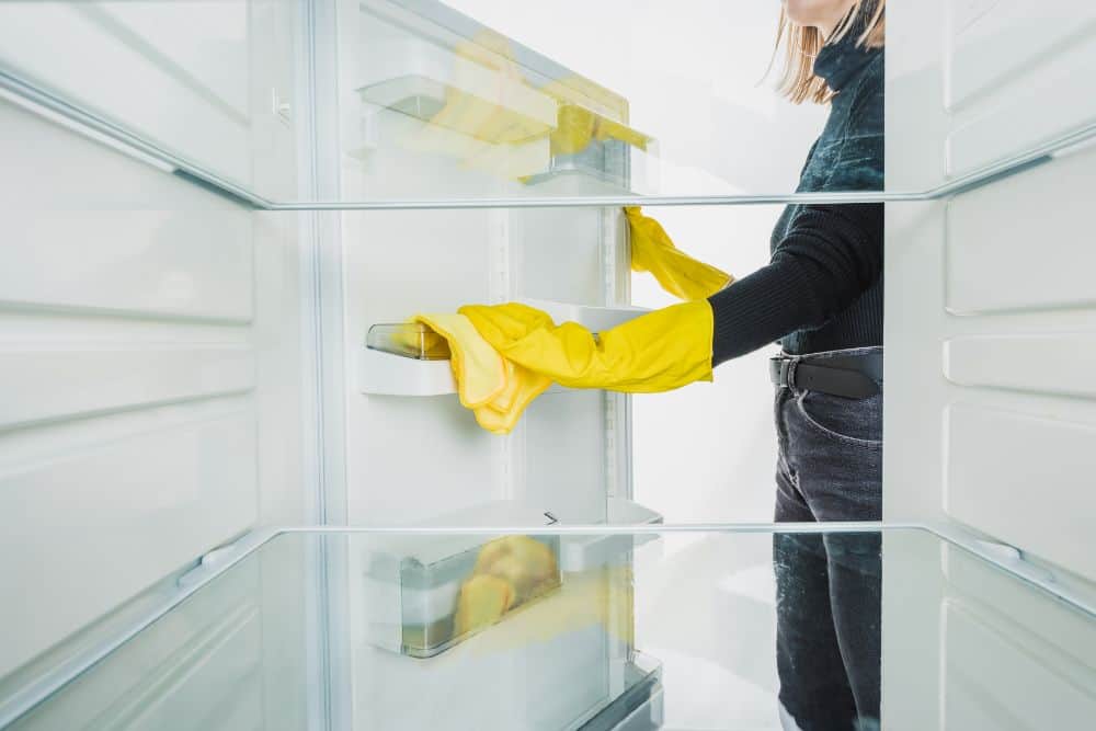 A woman wearing yellow gloves struggling with the strong suction of a refrigerator door.