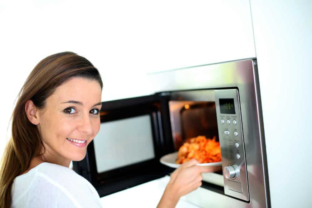 A woman holding a plate of food out of a microwave.